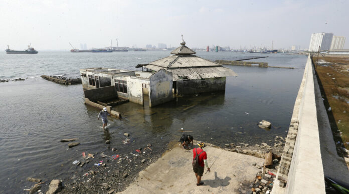 People walk near a giant sea wall which is used as a barrier to prevent sea water from flowing into land and cause flooding in Jakarta, Indonesia, Saturday, July 27, 2019. Photo: Achmad Ibrahim / AP