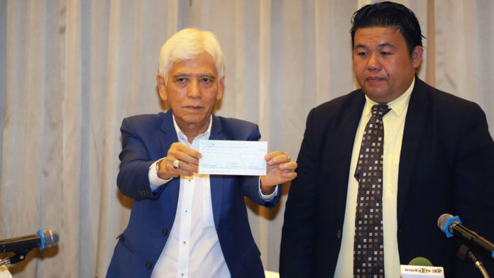 Suchai Thephasadin Na Ayudhya, left, holding a 500,000 cheque during a press conference on July 18 at Ploen restaurant. The clan’s lawyer Nattapol Thongkam, right, was also present.