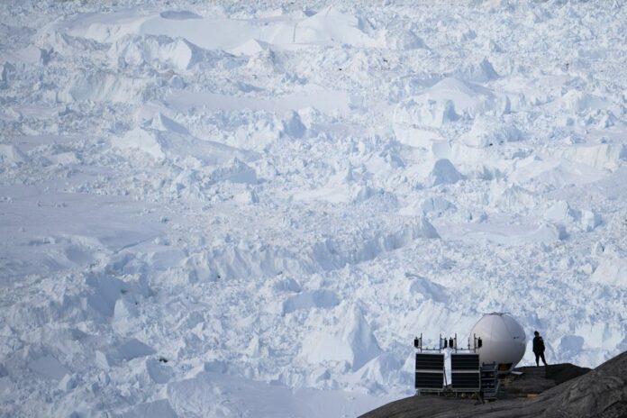 n this Aug. 16, 2019, photo, a woman stands next to an antenna at an NYU base camp at the Helheim glacier in Greenland. (AP Photo/Felipe Dana)