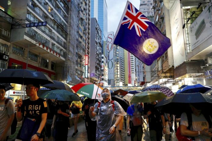 A protester waves a Hong Kong colonial-era flag as others march along a street in Hong Kong, Sunday, Aug. 18, 2019. (AP Photo/Vincent Yu)