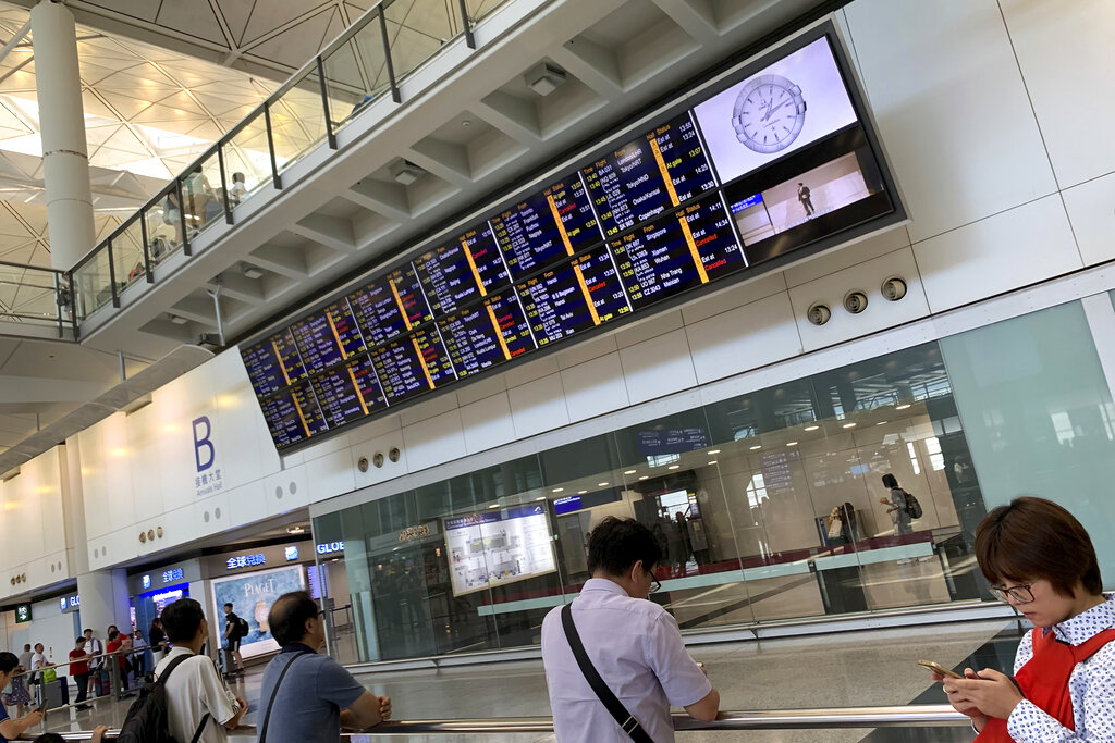 People wait near an electronic billboard showing some flight cancellation information at the arrival hall of Hong Kong International Airport in Hong Kong, Monday, Aug. 5, 2019. Hong Kong leader Carrie Lam maintained that she has no plans to resign in the face of a turbulent pro-democracy movement that held a general strike Monday leading to more than 100 flight cancellations and major traffic disruptions. Photo: Royston Chan / AP