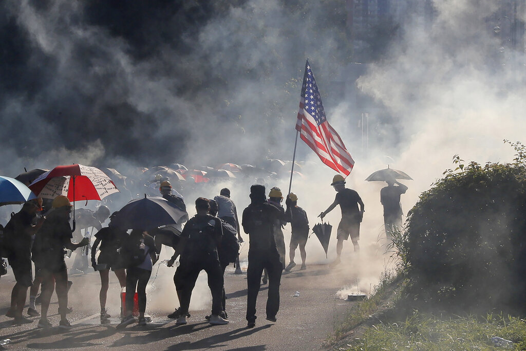 A protester runs with a United States flag as tear gas are released on protesters in Hong Kong on Monday, Aug. 5, 2019. Droves of protesters filled public parks and squares in several Hong Kong districts on Monday in a general strike staged on a weekday to draw more attention to their demands that the semi-autonomous Chinese city's leader resign. Photo: Kin Cheung / AP