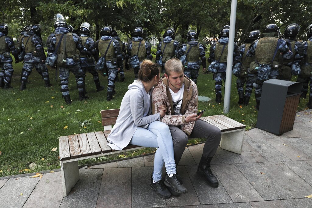 A couple sit in a boulevard as police walk to prevent protesters during a rally in Moscow, Russia, Saturday, Aug. 10, 2019. Tens of thousands of people rallied in central Moscow for the third consecutive weekend to protest the exclusion of opposition and independent candidates from the Russian capital's city council ballot. Photo: AP