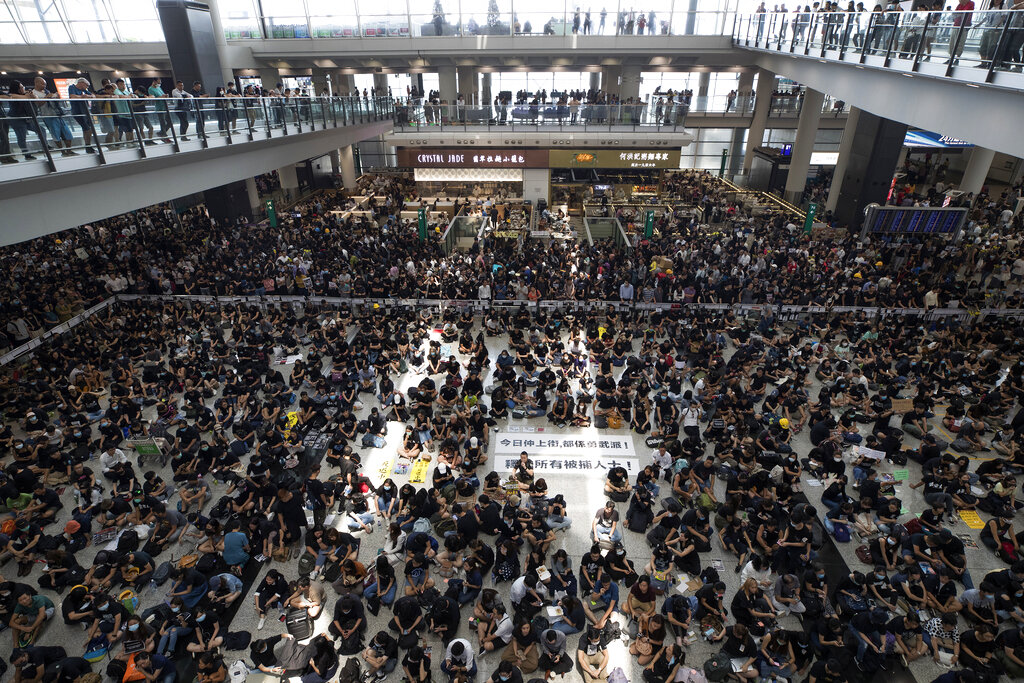 Protesters surround banners that read: "Those on the street today are all warriors!" center top, and "Release all the detainees!" during a sit-in rally at the arrival hall of the Hong Kong International airport in Hong Kong, Monday, Aug. 12, 2019. Hong Kong airport suspends check-in for all remaining flights Monday due to ongoing pro-democracy protest in terminal. Photo: Vincent Thian / AP