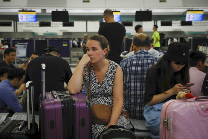 Australian Penny Tilley, center, reacts next to stranded travelers at the closed check-in counters at the Hong Kong International Airport, Monday, Aug. 12, 2019. One of the world's busiest airports canceled all flights after thousands of Hong Kong pro-democracy protesters crowded into the main terminal Monday afternoon. Photo: Kin Cheung / AP