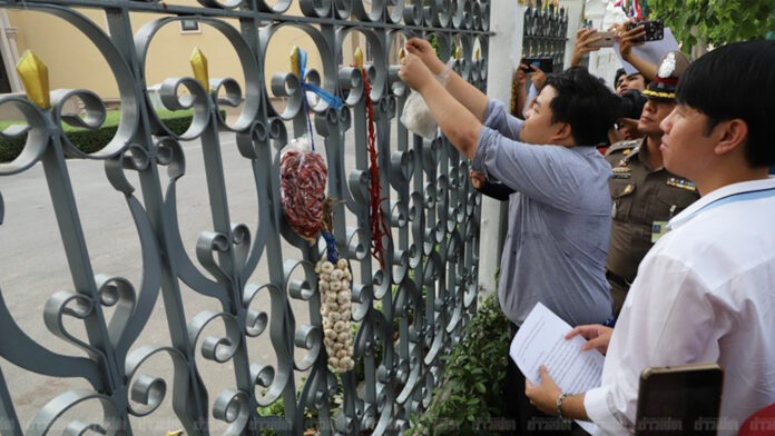 Parit “Penguin” Chiwarak, left, and Tanawat “Ball” Wongchai, right, hanging garlic and chili garlands on the fence of Government House on Feb. 2.