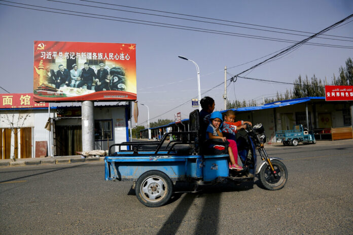 FILE - In this Sept. 20, 2018, file photo, an Uighur woman shuttles school children on an electric scooter as they ride past a propaganda poster showing China's President Xi Jinping joining hands with a group of Uighur elders in Hotan, in western China's Xinjiang region. The Trump administration, locked in a trade war with China, is increasing the pressure on Beijing over what it says is the systematic oppression of ethnic minority Muslims. American officials hosted a panel Tuesday, Sept. 24, 2019, on the sidelines of the United Nations General Assembly gathering in New York to highlight the plight of Uighurs, whose native land in China’s far western Xinjiang province they say is a police state. Photo: Andy Wong / AP File