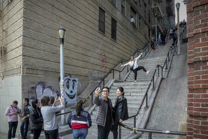 People pose on the steps between two apartment buildings, Monday Oct. 28, 2019, in the Bronx borough of New York. The stairs have become a tourist attraction in recent weeks since the release of the movie “Joker.” In the movie, lead actor Joaquin Phoenix dances as he goes down the steps, wearing a bright red suit and clown makeup. (AP Photo/Bebeto Matthews)