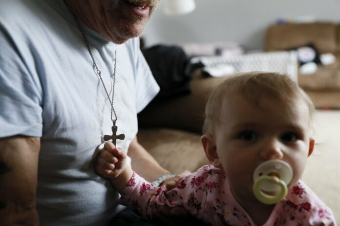 In this Nov. 28, 2018, file photo Annabella Wolikow, 10-month-old daughter of Tom Wolikow, holds her grandfather John's crucifix necklace at their home in Warren, Ohio. An economic renaissance in the industrial Midwest promised by President Donald Trump has suffered in recent weeks in ways that could be problematic for Trump's 2020 re-election. (AP Photo/John Minchillo, File)