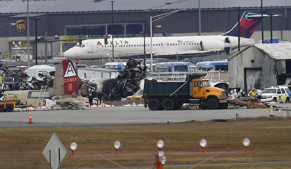 A Delta commercial airline plane taxis to take-off behind investigators at the wreckage of World War II-era bomber plane that crashed at Bradley International Airport in Windsor Locks, Conn., Wednesday, Oct. 2, 2019. Photo: Jessica Hill / AP