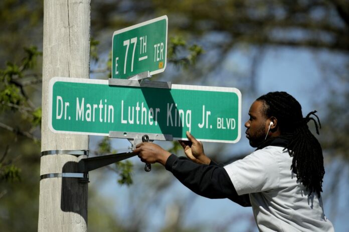 In this April, 20, 2019, file photo, public works employee Jerry Brooks changes a street sign from The Paseo to Dr. Martin Luther King Jr. Blvd. in Kansas City, Mo. (AP Photo/Charlie Riedel, File)