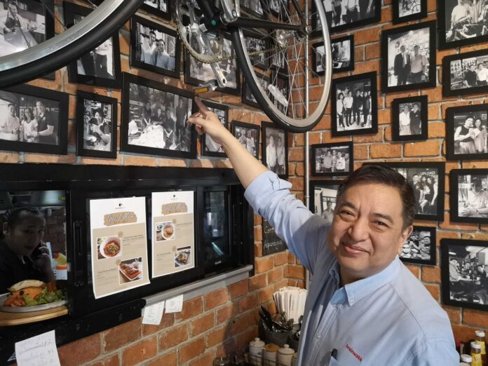 Suranand Vejjajiva points to photos of prominent clients of Brainwake Cafe.