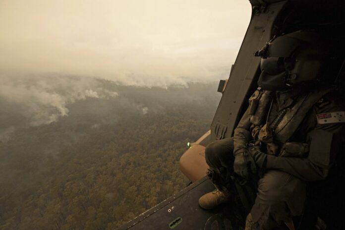 In this Sunday, Jan. 5, 2020, photo provided by Australian Department of Defence, a Royal Australian Navy MRH-90 helicopter crew member looks out over fires burning near Cann River, Australia. The wildfires have so far scorched an area twice the size of the U.S. state of Maryland. (Private Michael Currie/ADF via AP)
