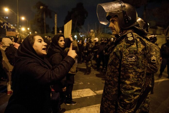 In this Saturday, Jan. 11, 2020 photo, released by Iranian Students' News Agency, ISNA, a woman attending a candlelight vigil to remember the victims of the Ukraine plane crash, talks to a policeman, at the gate of Amri Kabir University in Tehran, Iran. (Mona Hoobehfekr/ISNA via AP)