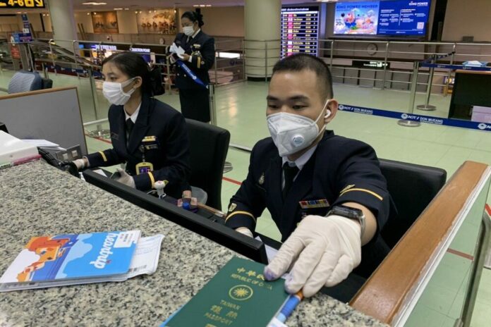 An immigration police officer wears a mask as he inspects a Taiwanese tourist's travel document at Don Mueang Airport on Jan. 26, 2020.