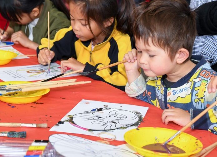 Children fill Peking Opera mask paintings with colors at an activity of