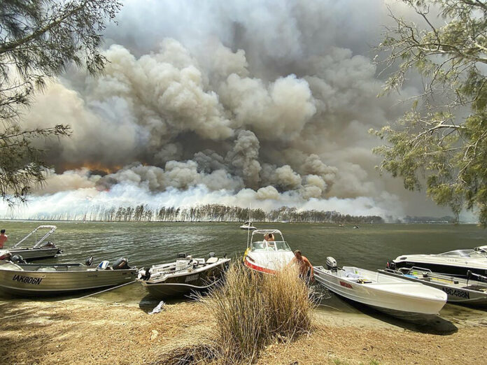 Boats are pulled ashore as smoke and wildfires rage behind Lake Conjola, Australia, Thursday, Jan. 2, 2020. Thousands of tourists fled Australia's wildfire-ravaged eastern coast Thursday ahead of worsening conditions as the military started to evacuate people trapped on the shore further south. Photo: Robert Oerlemans via AP