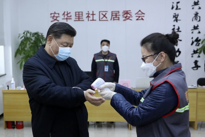 In this photo released by Xinhua News Agency, Chinese President Xi Jinping, left, wearing a protective face mask, receives a temperature check as he visits a community health center in Beijing, Monday, Feb. 10, 2020. (Pang Xinglei/Xinhua via AP)