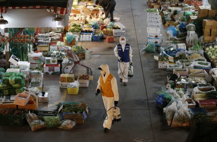 Workers wearing a protective suit spray disinfectant as a precaution against the COVID-19 at a market in Seoul, South Korea, Thursday, Feb. 27, 2020. (AP Photo/Lee Jin-man)