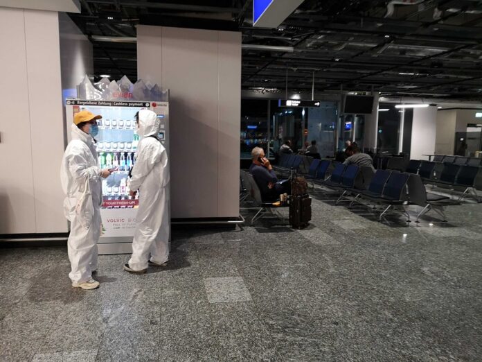 At Frankfurt Airport, two Chinese passengers wearing protection suits buy drinks from a vending machine. They were denied from boarding a flight to Bangkok for a lack of coronavirus test certificate and health insurance.