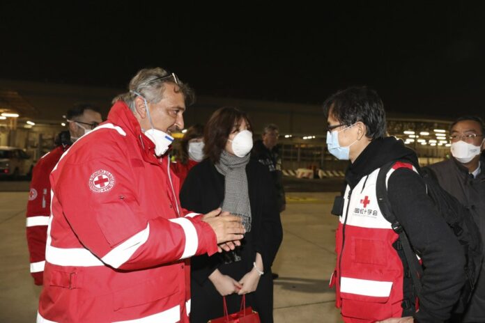 In this photo released by China's Xinhua News Agency, Francesco Rocca, left, the National President of the Italian Red Cross Association, greets members of a Chinese aid team as they arrive at Fiumicino Airport in Rome, late Thursday, March 12, 2020. (Cheng Tingting/Xinhua via AP)