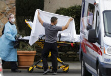 Anxiety Grips Companies Across the World as Virus Spreads In this Feb. 29, 2020, file photo, a staff member blocks the view as a person is taken by a stretcher to a waiting ambulance from a nursing facility where people are sick and being tested for the COVID-19 virus in Kirkland, Wash. From Miami to Seattle, nursing homes and other facilities for the elderly are stockpiling masks and thermometers, preparing for staff shortages and screening visitors to protect a particularly vulnerable population from the deadly new coronavirus. Photo: Elaine Thompson / AP File