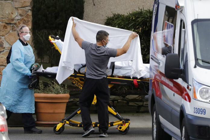 In this Feb. 29, 2020, file photo, a staff member blocks the view as a person is taken by a stretcher to a waiting ambulance from a nursing facility where people are sick and being tested for the COVID-19 virus in Kirkland, Wash. From Miami to Seattle, nursing homes and other facilities for the elderly are stockpiling masks and thermometers, preparing for staff shortages and screening visitors to protect a particularly vulnerable population from the deadly new coronavirus. Photo: Elaine Thompson / AP File