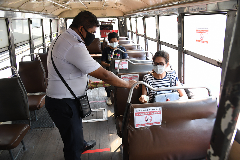 Seats on a Bangkok bus are marked with signs instructing passengers to leave a space for social-distancing.