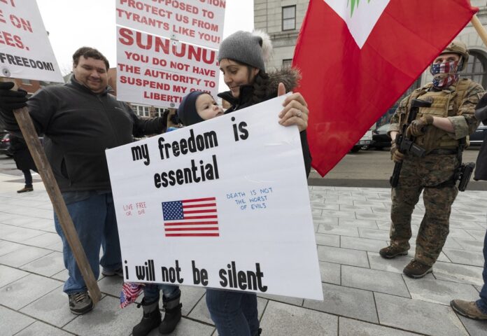 A protester holds a sign with her son during a demonstration against the government mandated lockdown due to concern about COVID-19 at the State House, Saturday, April 18, 2020, in Concord, N.H. (AP Photo/Michael Dwyer)