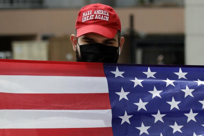 Sevag Demirjian, a supporter of President Trump, waves an American flag at passing demonstrators during a protest outside of the Edward R. Roybal Federal building Tuesday, March 31, 2020, in Los Angeles. (AP Photo/Marcio Jose Sanchez)