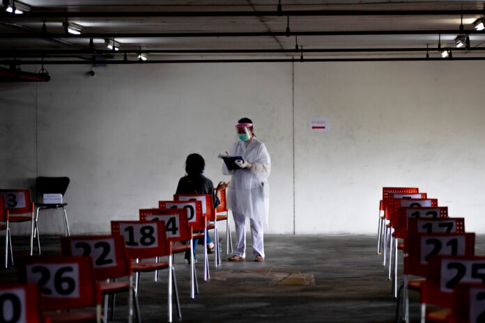 A nurse in protective clothing takes notes from a woman with symptoms of new coronavirus at a carpark that turned into a COVID-19 infection screening center at Chulalongkorn University's Health Service Center on April 1, 2020. Photo: Gemunu Amarasinghe / AP