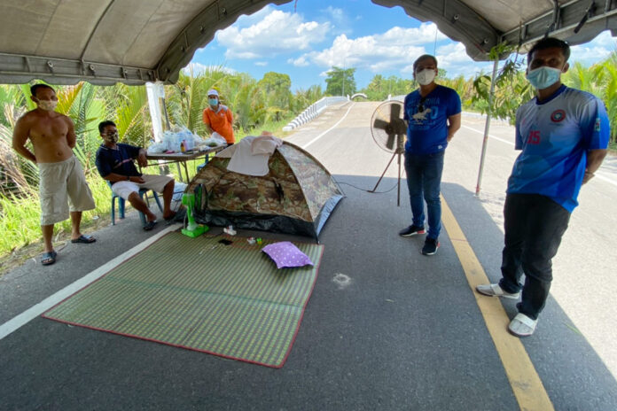 Thai workers returning from Malaysia stand by a tent at a quarantine facility in Trang’s Kantang district on April 2, 2020. Thai workers returning from Malaysia stand by a tent at a quarantine facility in Trang’s Kantang district on April 2, 2020.