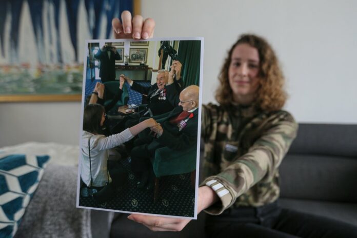 In this photo taken on Tuesday May 5 2020, Marion Nivard, 15, a student at Saint-Louis Middle School in Cabourg, shows a photo of WWII veterans, including Bill Ridgewell, in Varaville, Normandy.As V-E Day approached, Nivard and her classmates in the Normandy region thought of 94-year-old Bill Ridgewell and other vets living in isolation because of the COVID-19 pandemic — just as they were. The teens decided to swap stories with the men about their lives under lockdown. Photo: David Vincent / AP