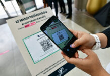 3 New Infections Found, Gov’t Urges Wider Use of Tracing Site A customer at Siam Paragon uses her phone to scan the QR code logging her visit with a government website on May 17, 2020.