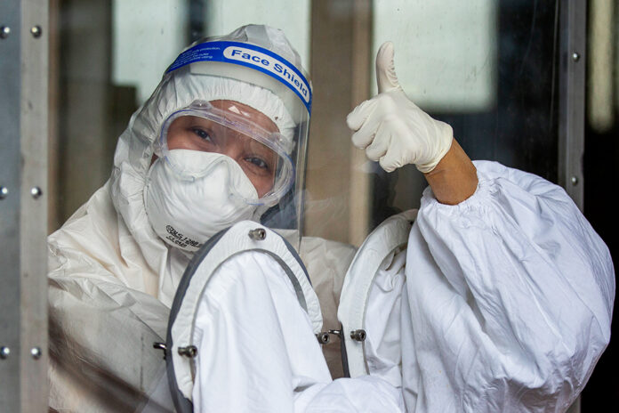 A health worker in protective clothing gives thumbs up from behind a plastic partition as she prepares to collect nasal swab samples to test for the coronavirus in Bangkok, Thailand, Wednesday, May 6, 2020. Photo: Gemunu Amarasinghe / AP
