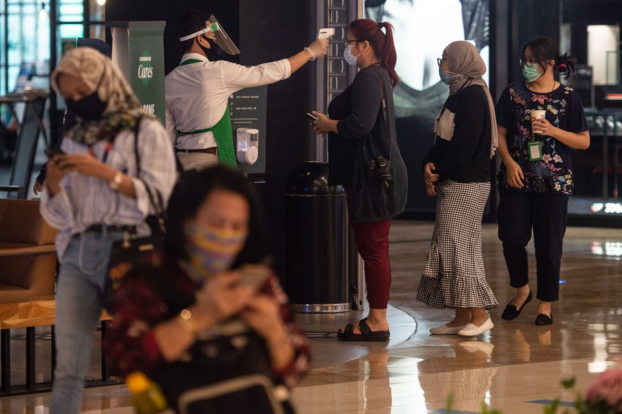 A staff member checks the body temperature of a visitor at a reopened shopping mall in Jakarta, Indonesia, June 15, 2020. Photo: Veri Sanovri / Xinhua