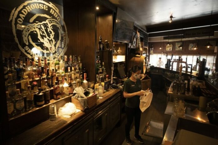 A worker wearing a face mask to help curb the spread of the coronavirus as she cleans a glass in front of the bar area at Roadhouse Barbecue restaurant in Bangkok, Thailand, Monday, June 15, 2020. Photo: Sakchai Lalit / AP
