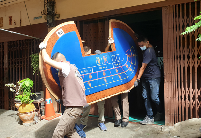 Police carry a baccarat table on Aug. 10, 2020, part of a hidden stash from a gambling den in the Rama III area where four people were killed Aug. 4, 2020.