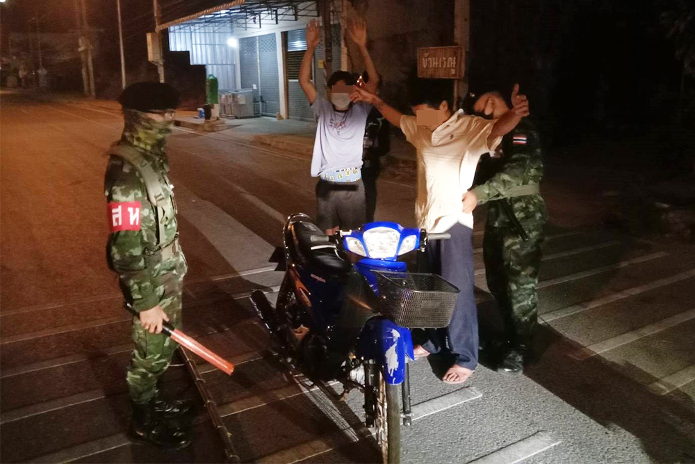 Military police officers search a man who is stopped for violating the curfew in Suphan Buri province on April 28, 2020.