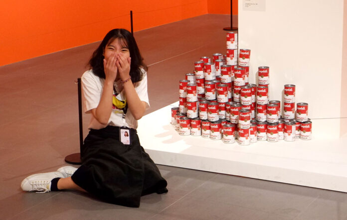 A Thai woman giggles next to a stack of Campbell’s Soup Cans at the first Andy Warhol exhibition in Thailand on Aug. 11, 2020.