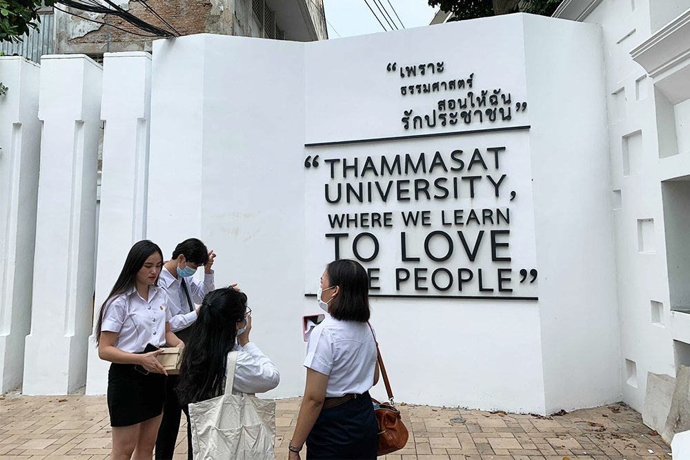 Students stand by the iconic sign of the university's unofficial motto.