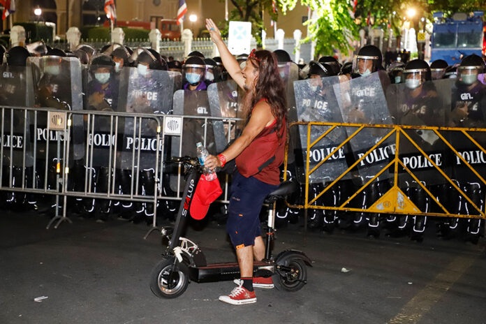 A man raises a three-finger salute as riot police disperse protesters outside Government House on Oct. 15, 2020.