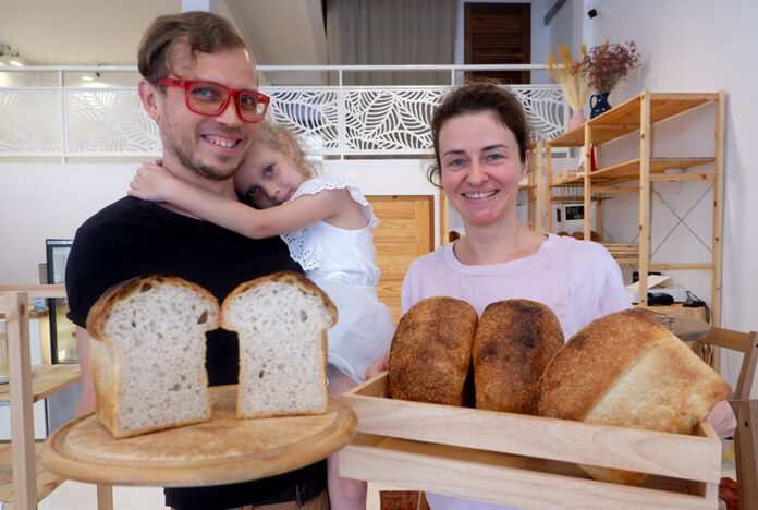 Andrei Matveenkov, Daria Matveenkova, 5, and Olga Matveenkova holding loaves of sourdough bread.