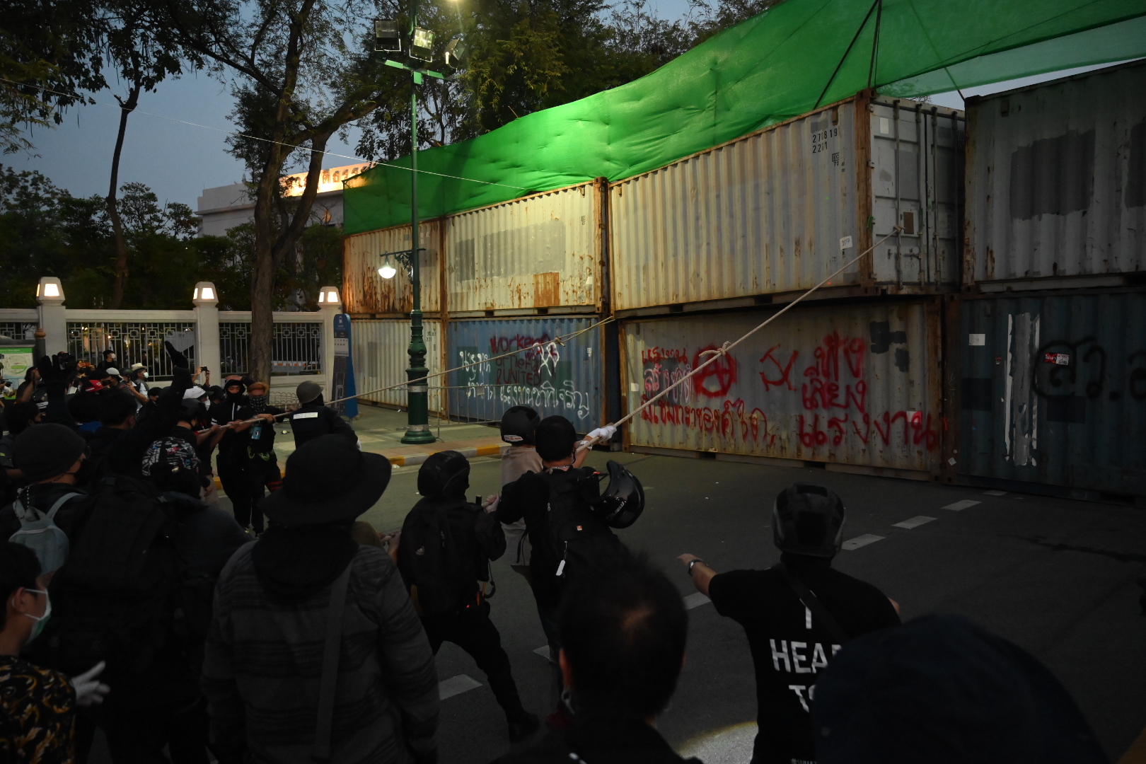 Protesters pull down a shipping container used as a barricade near the Grand Palace on Mar. 20, 2021.