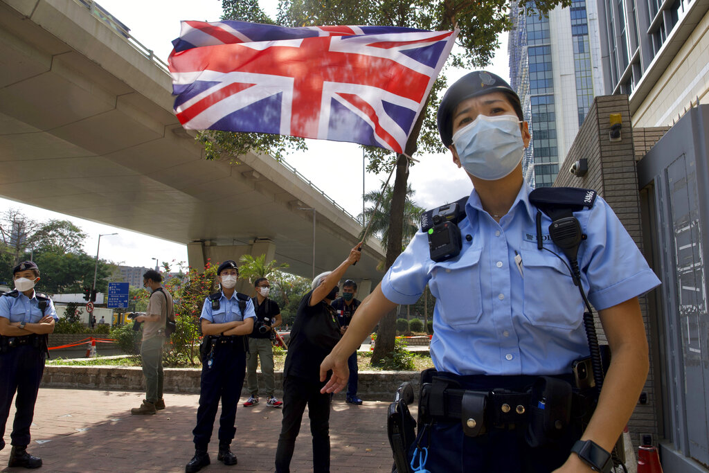 A pro-democracy supporter waves a British flag as police officers stand guard outside a court in Hong Kong Thursday, April 1, 2021. Photo: Vincent Yu / AP