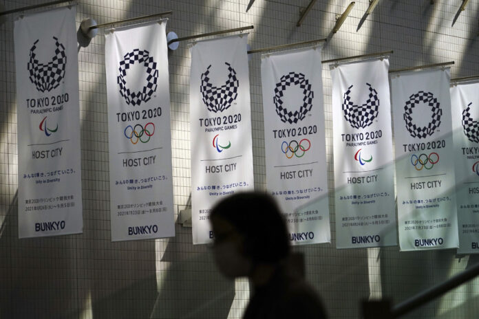 A woman wearing a protective mask to help curb the spread of the coronavirus walks near banners for Tokyo 2020 Olympic and Paralympic Games Wednesday, March 31, 2021. Photo: Eugene Hoshiko / AP