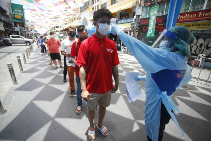 A health worker checks the temperature of a man falling in line for a COVID-19 swab test in Khaosan Road in Bangkok, Thailand Wednesday, April 14, 2021. Photo: Somchai Chanjirakitti / AP