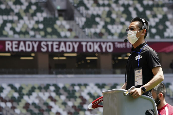 An official wears a face mask as he uses a starter pistol to signal the start a women's 100 meter heat at an athletics test event for the Tokyo 2020 Olympics Games at National Stadium in Tokyo, Sunday, May 9, 2021. Photo: Shuji Kajiyama / AP