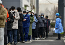 China’s Tianjin on Partial Lockdown After Omicron Found In this photo released by Xinhua News Agency, a worker wearing a protection suit looks at residents wearing face masks to protect from the coronavirus as they line up for the coronavirus test during a mass testing in north China's Tianjin municipality, Sunday, Jan. 9, 2022. Photo: Zhao Zishuo / Xinhua via AP