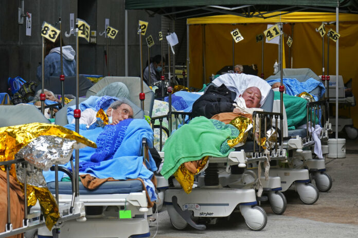 Patients lie on hospital beds as they wait at a temporary holding area outside Caritas Medical Centre in Hong Kong Wednesday, Feb. 16, 2022. Photo: Vincent Yu / AP Patients lie on hospital beds as they wait at a temporary holding area outside Caritas Medical Centre in Hong Kong Wednesday, Feb. 16, 2022. Photo: Vincent Yu / AP